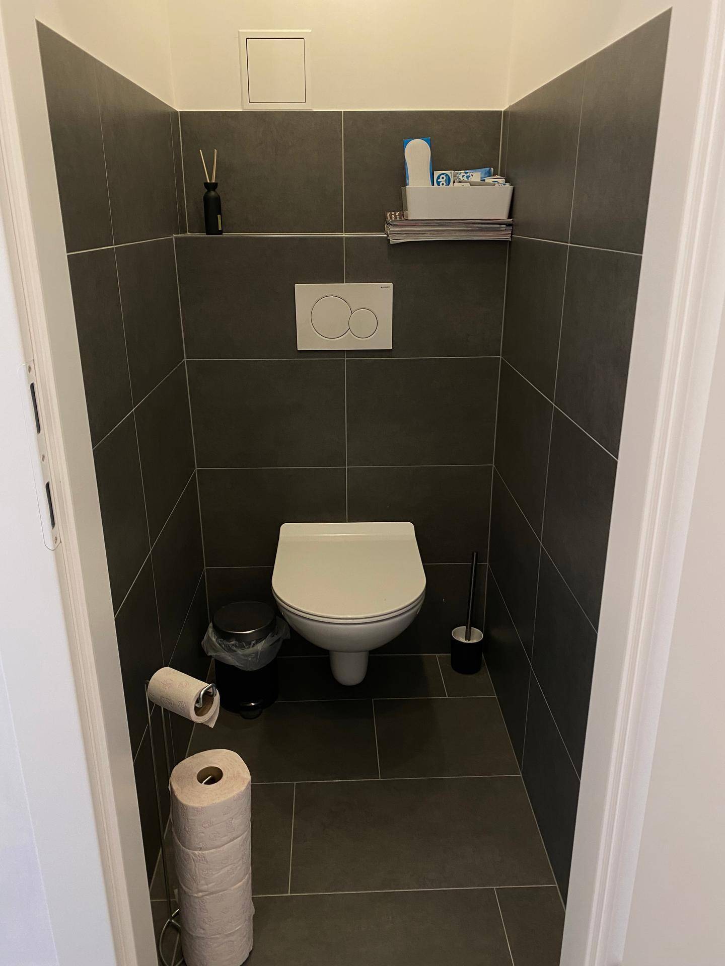 Separates WC mit Wand-WC und dunklen Fliesen, minimalistisch und funktional.
