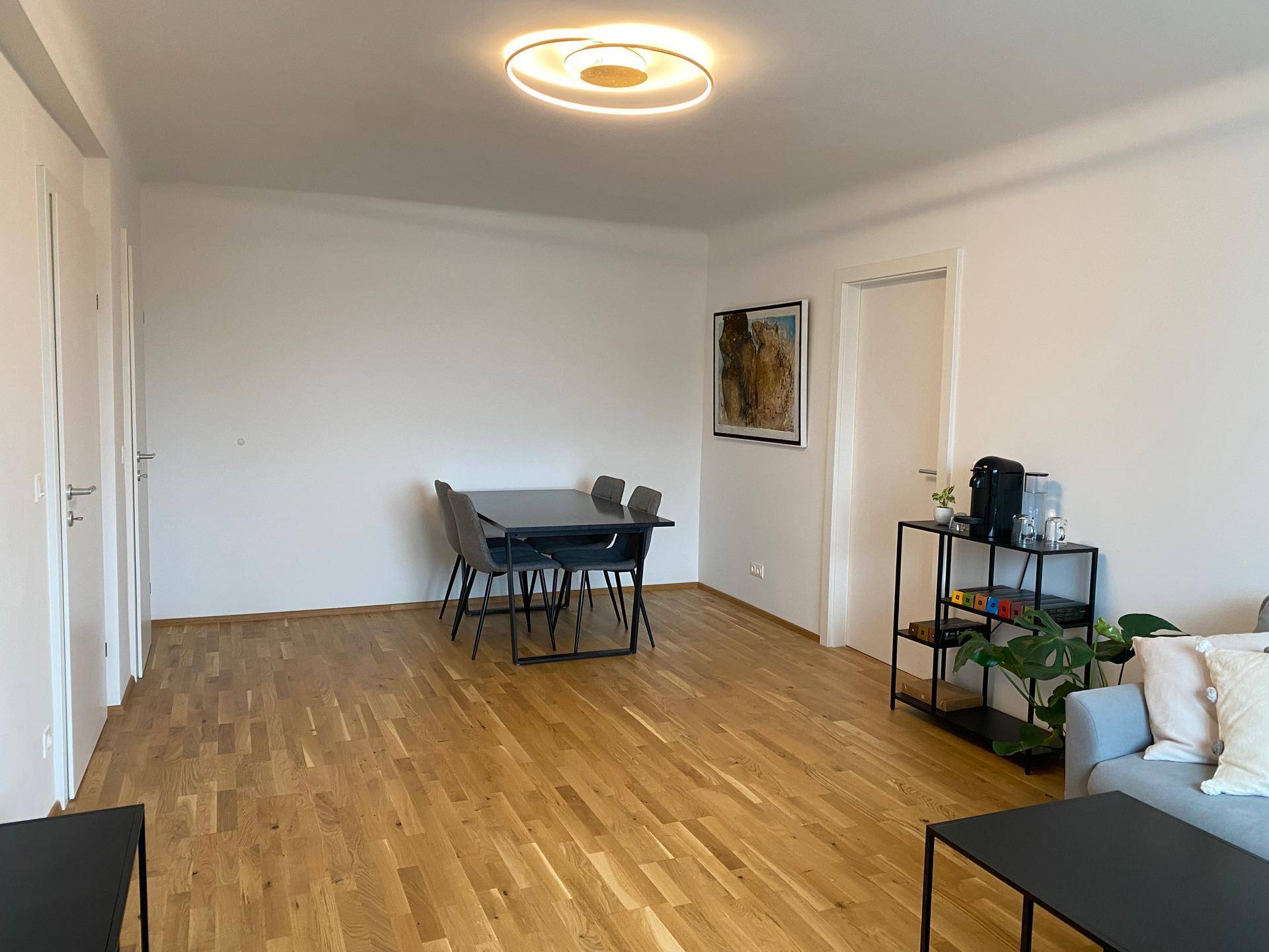 Offener Wohn-Essbereich mit Parkettboden, Esstisch und moderner Deckenleuchte.
