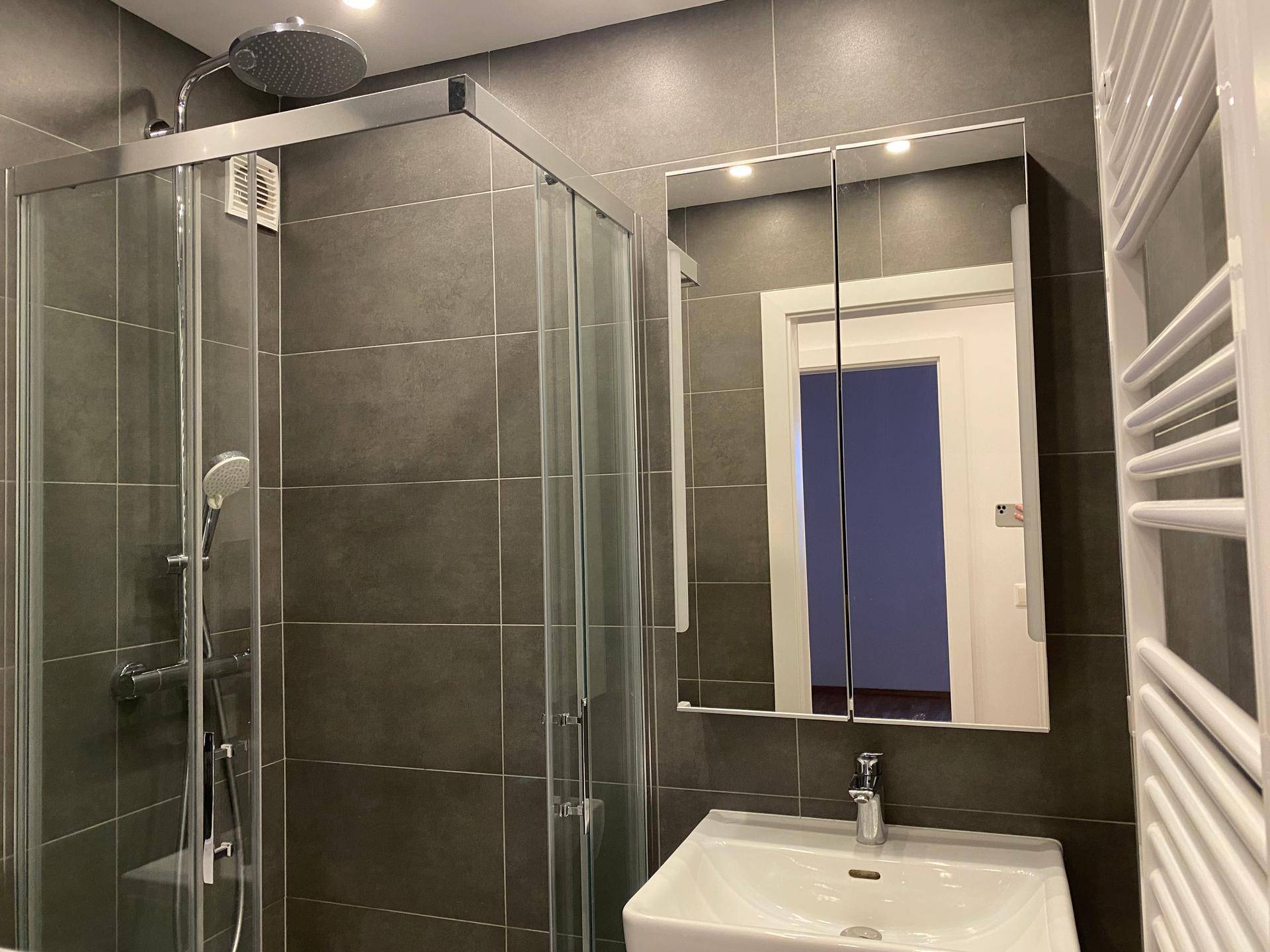 Zeitgemäßes Badezimmer mit Duschkabine, Waschbecken und beheiztem Handtuchhalter.