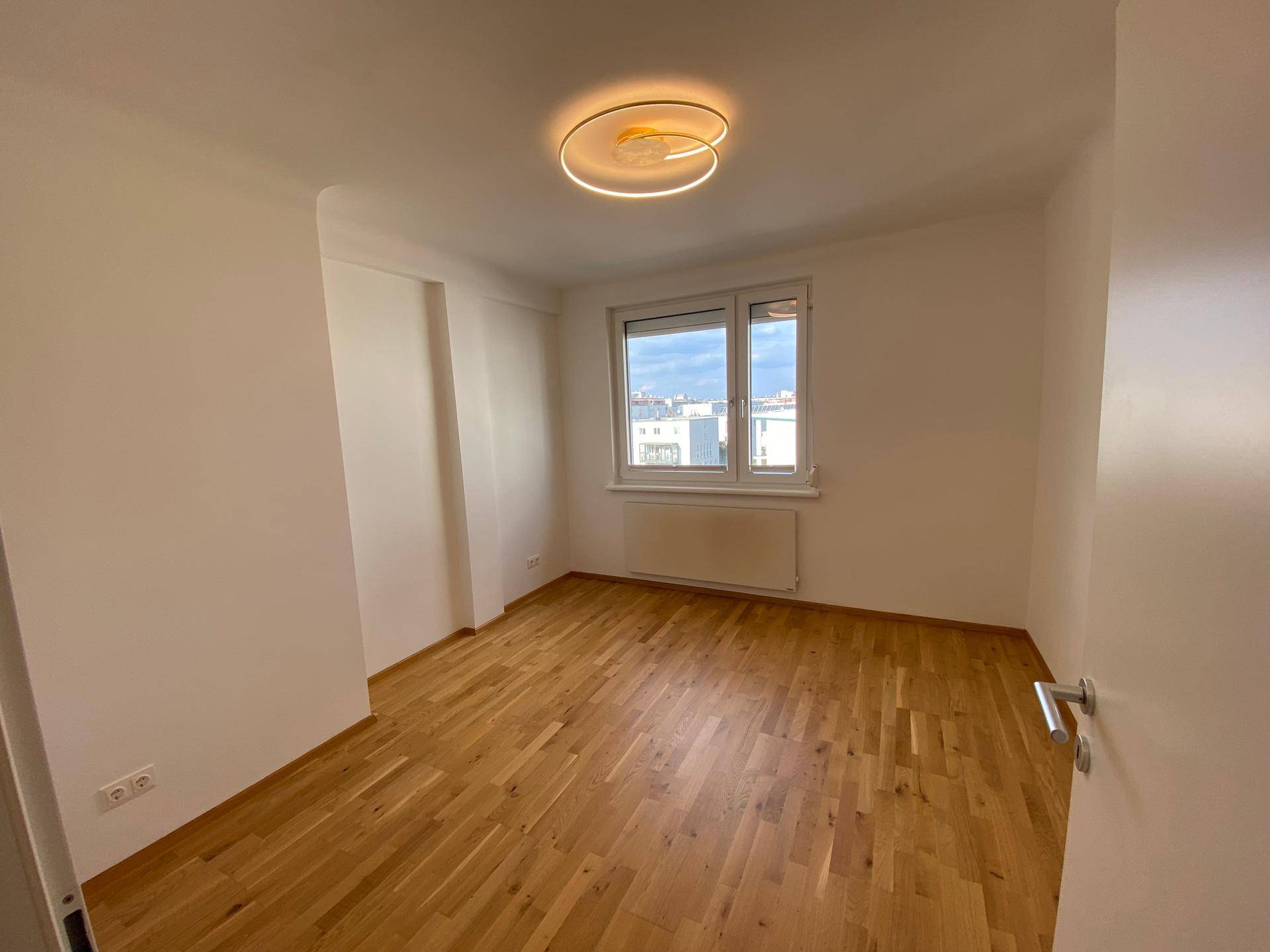 Geräumiges Zimmer mit Parkettboden und großem Fenster, bietet Weitblick über die Stadt.