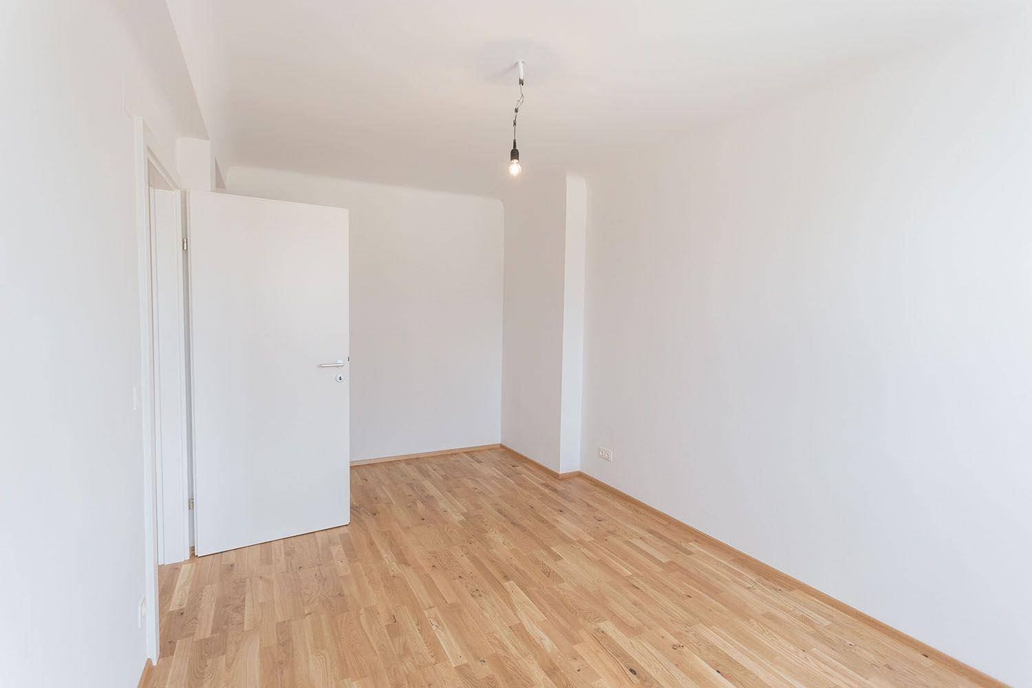 Leeres Zimmer mit Parkettboden und weiß gestrichenen Wänden, bereit zur individuellen Gestaltung.