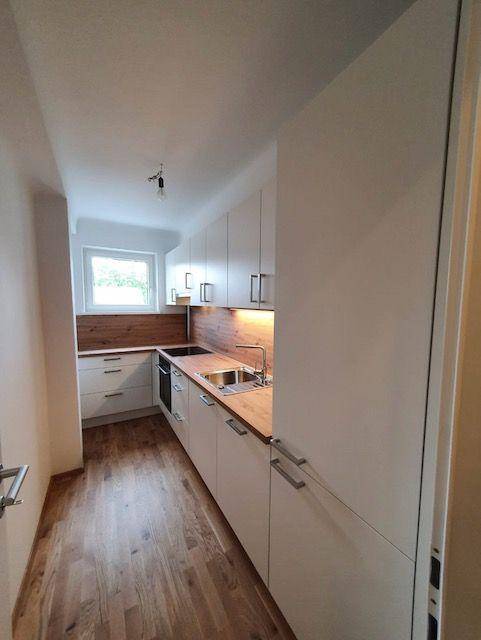 Moderne Küche mit weißen Schränken, Holz-Arbeitsplatte und Fenster für Tageslicht.