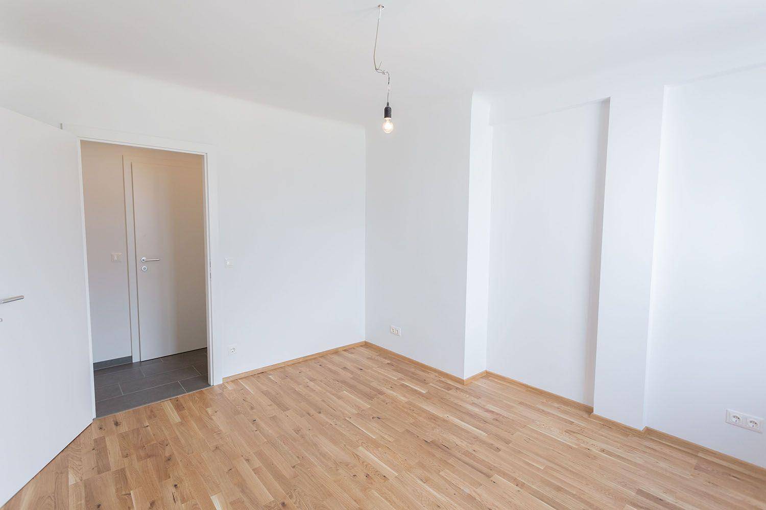 Geräumiges Zimmer mit Parkettboden und Zugang zum gefliesten Flurbereich.