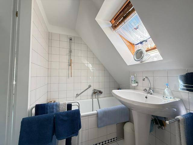 Badezimmer mit Badewanne, Waschbecken und Dachfenster unter einer Dachschräge.