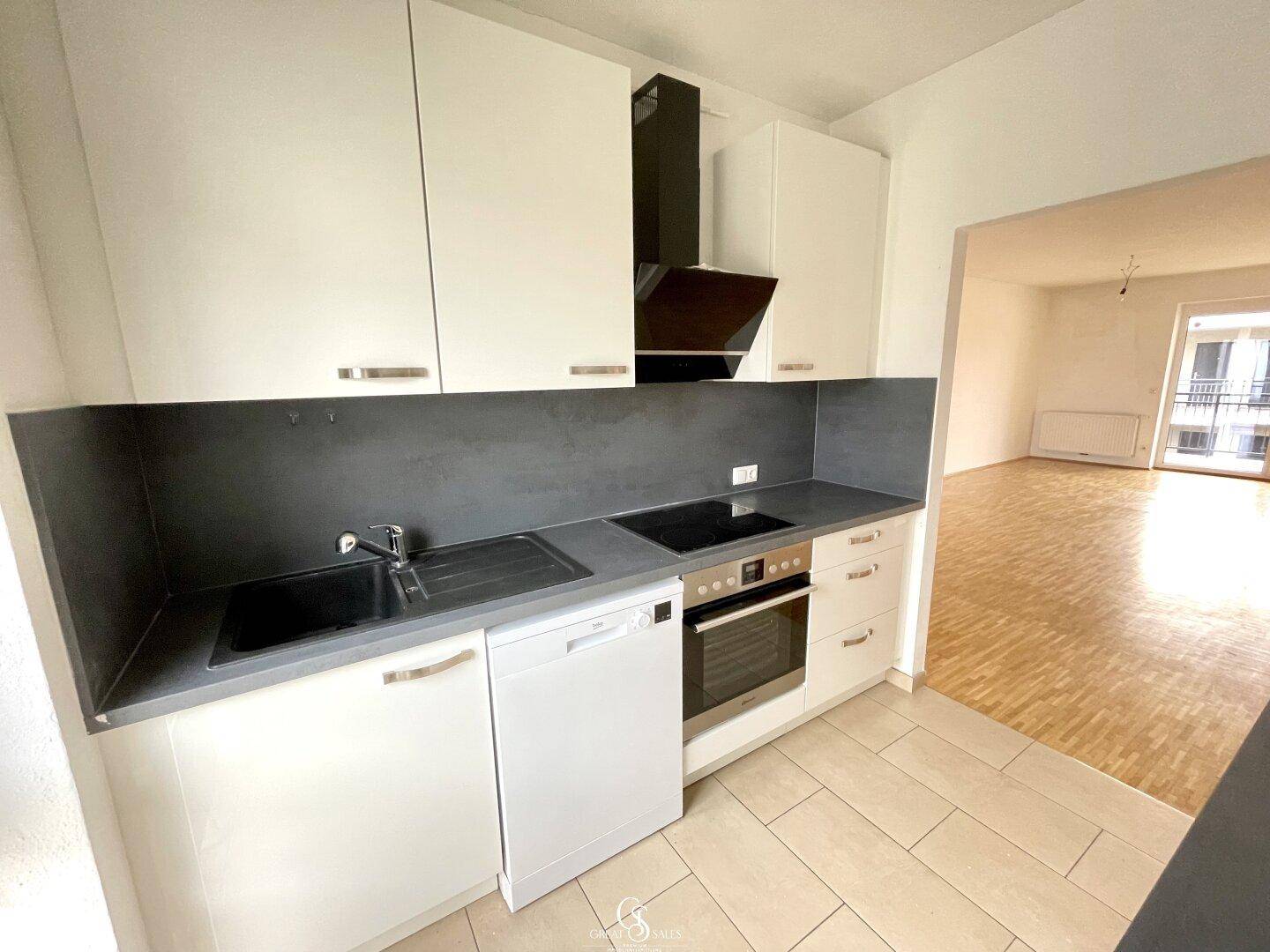 Funktionale Küche mit weißen Schränken, dunkler Arbeitsplatte und Blick in den Wohnbereich.