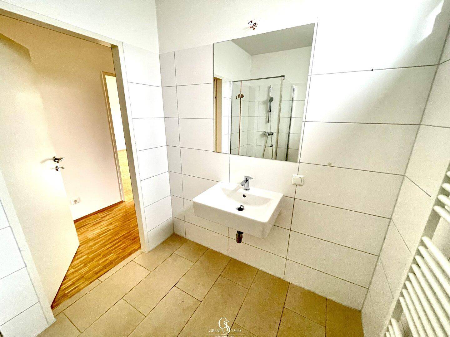 Modernes Badezimmer mit weißen Fliesen, Waschbecken und Spiegel, offen zum Schlafzimmer.