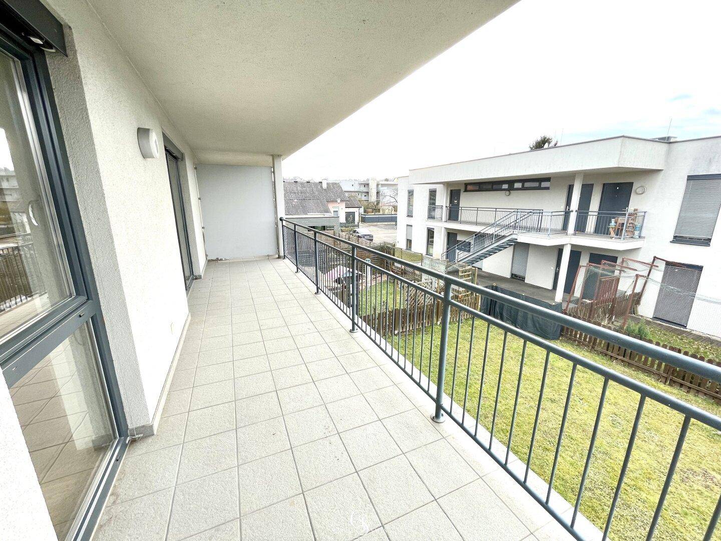 Langer Balkon mit Fliesenboden und Metallgeländer, bietet Blick auf die umliegenden Gebäude.