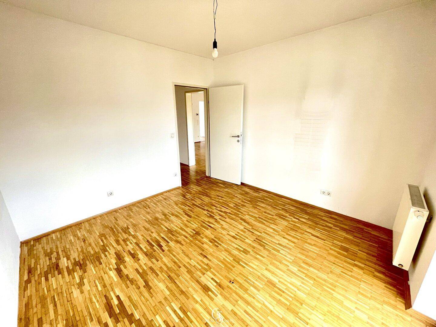 Leeres Schlafzimmer mit Parkettboden und weiß gestrichenen Wänden, ideal für individuelle Gestaltung.