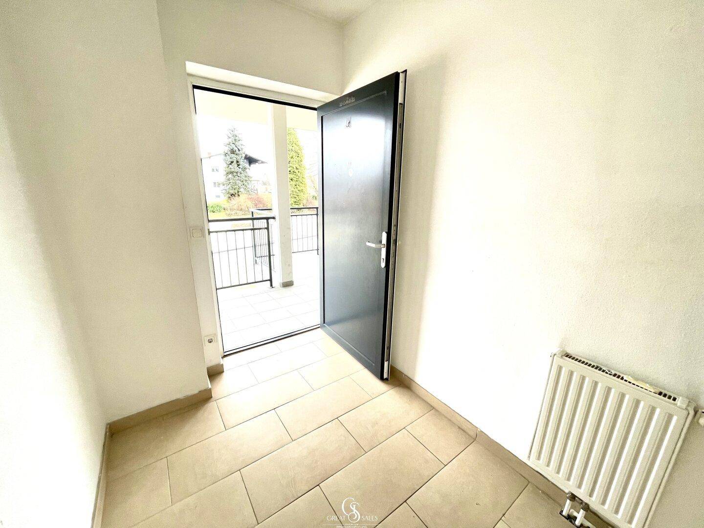 Heller Eingangsbereich mit Fliesenboden und offener Tür, die zum Außenbereich und Balkon führt.