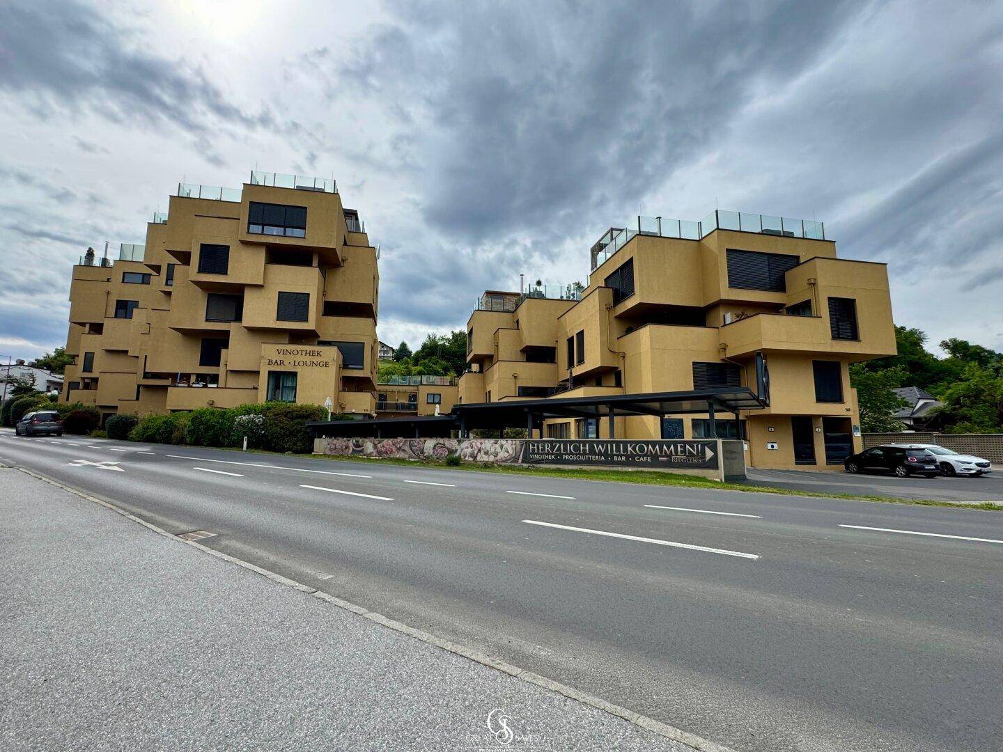 Moderne Wohnanlage mit markanter Architektur und Geschäften im Erdgeschoss an einer Straße.