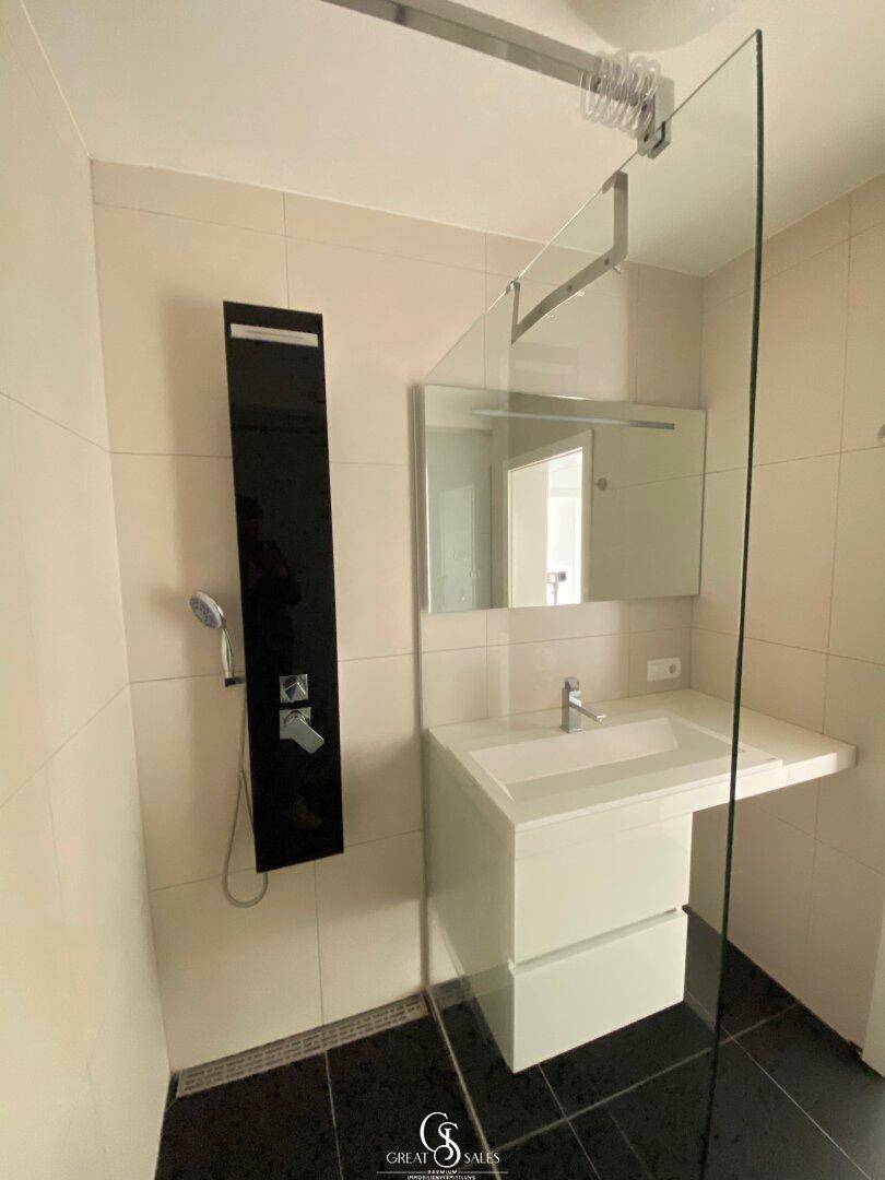 Modernes Badezimmer mit Glasdusche, Einzelwaschbecken und dunklem Fliesenboden.