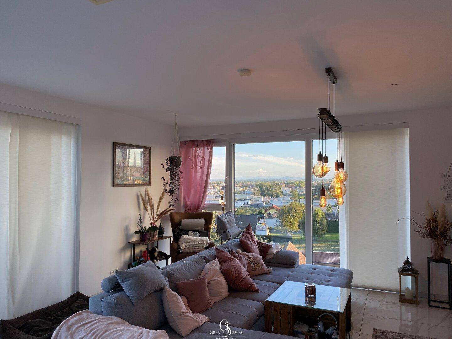 Gemütliches Wohnzimmer mit großem Sofa, modernen Leuchten und weitem Ausblick.