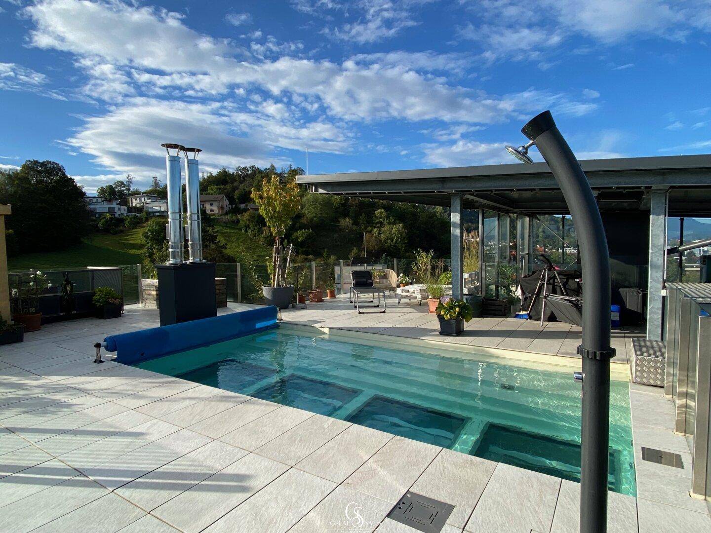 Großzügige Dachterrasse mit Pool, Außendusche und weitem Blick unter blauem Himmel.