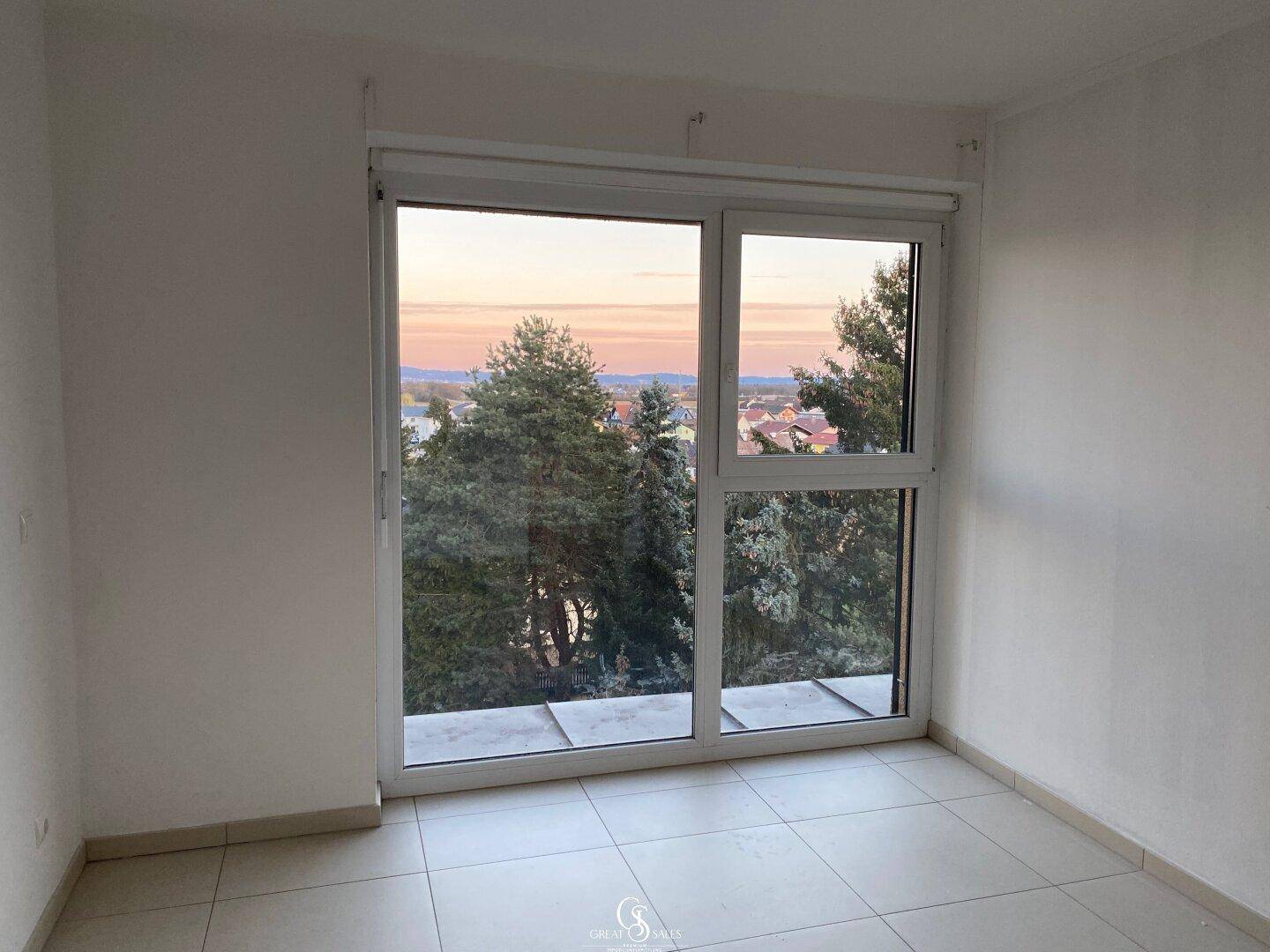 Leeres Schlafzimmer mit großen Fenstern und Blick auf die umliegende Landschaft.