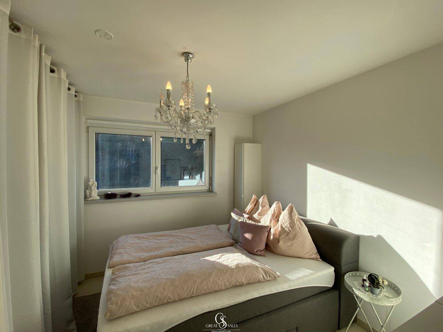 Helles Schlafzimmer mit Doppelbett, Kronleuchter und Fenster mit Blick nach draußen.