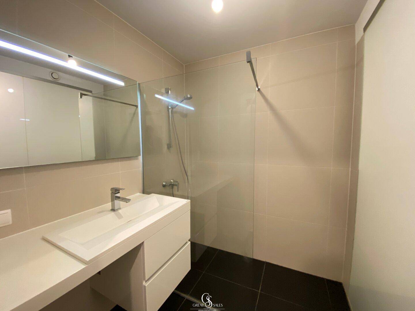 Modernes Badezimmer mit begehbarer Dusche, Einzelwaschbecken und beigen Fliesen.