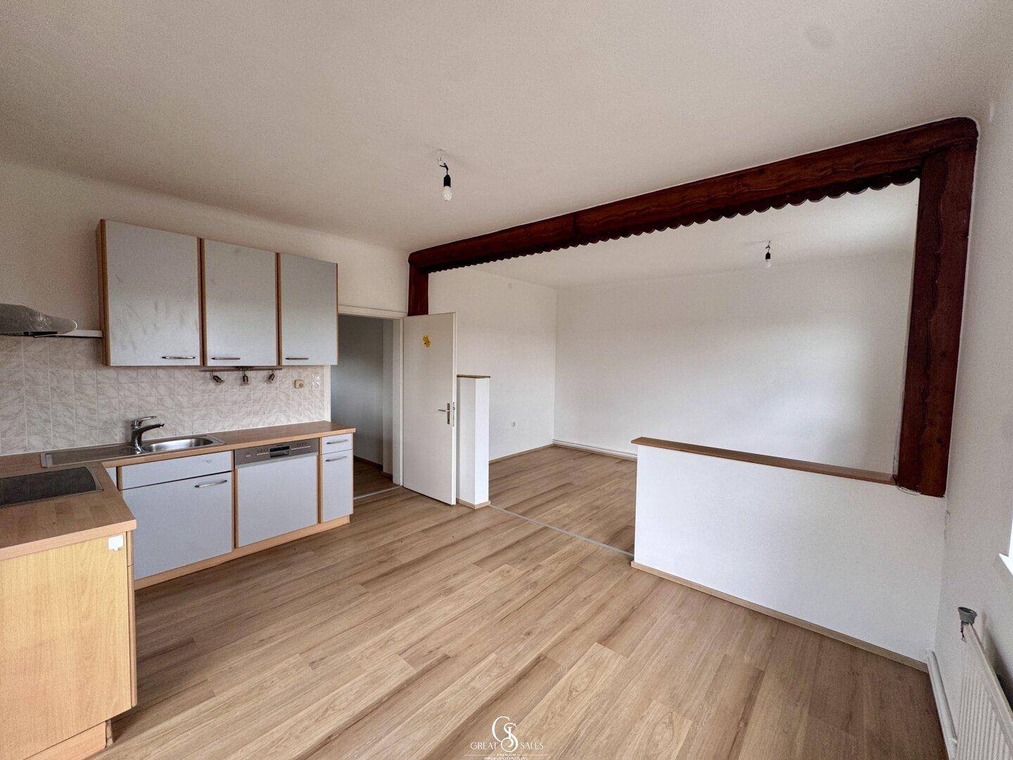 Offene Küche mit Holztheke und Blick in den angrenzenden Wohnbereich mit rustikalem Holzbalken.