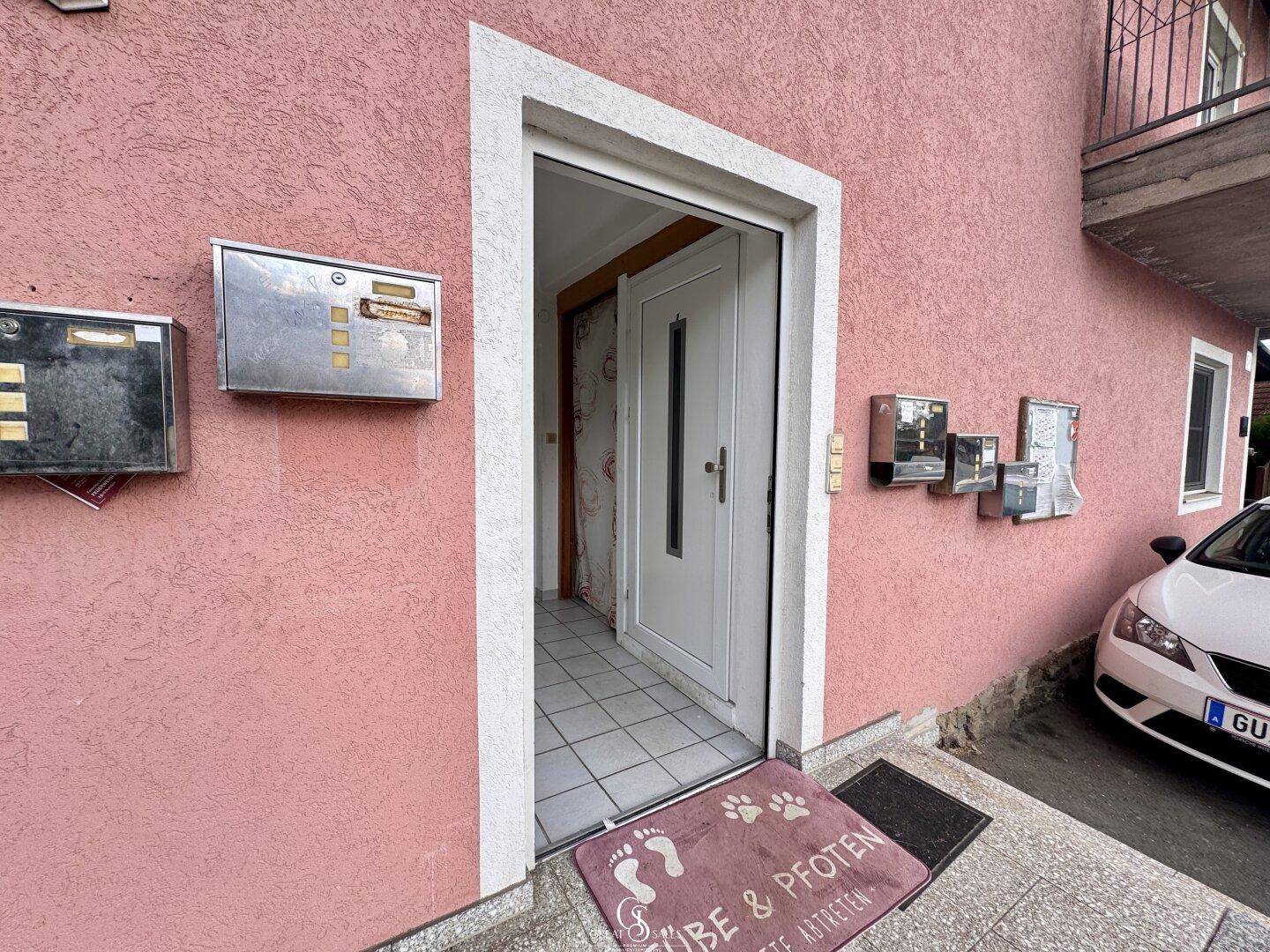 Eingangsbereich des Hauses mit rosa Fassade, weißer Tür und mehreren Briefkästen an der Wand.