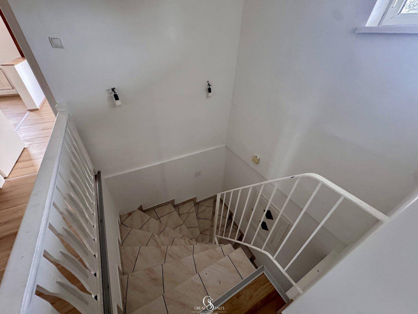 Treppenhaus mit gefliesten Stufen und weißem Geländer, das in die untere Etage führt.