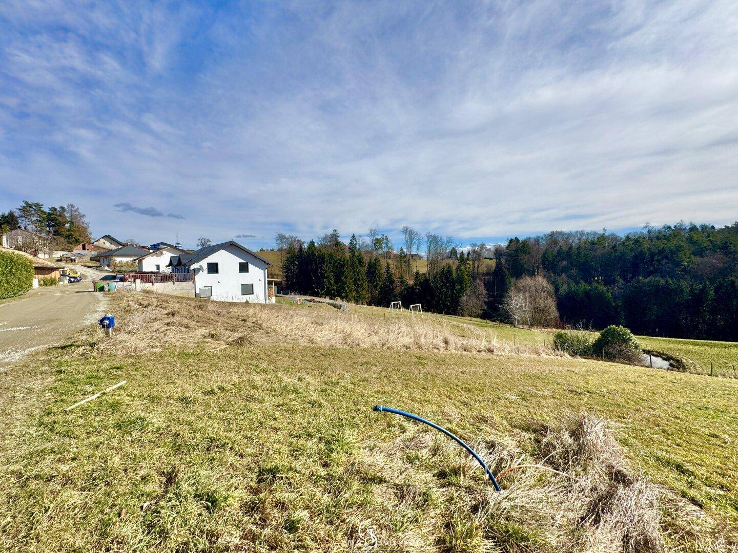 Weite Grasfläche mit einem modernen weißen Haus am Rand und einem blauen Rohr im Vordergrund.