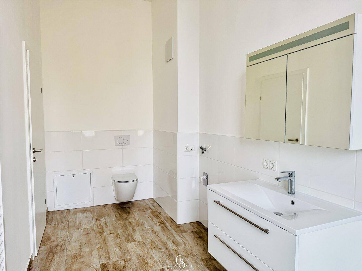 Modernes Badezimmer mit wandhängendem WC, Einzelwaschbecken und großem Spiegelschrank.