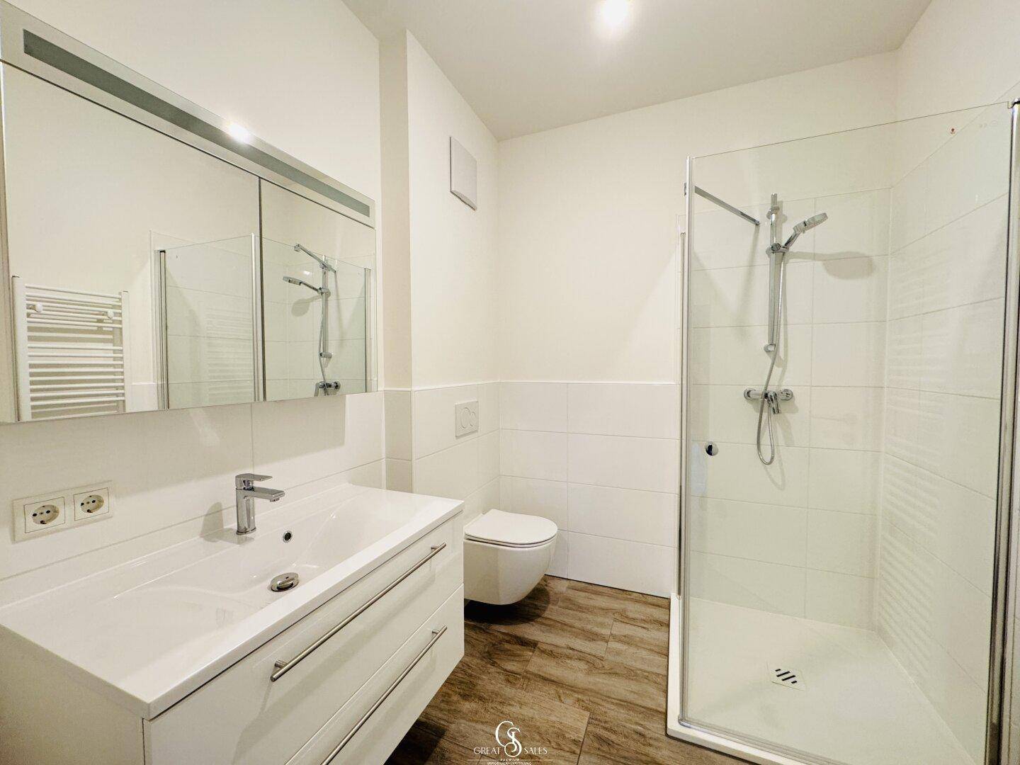 Helles Badezimmer mit ebenerdiger Dusche, Einzelwaschbecken und beheiztem Handtuchhalter.