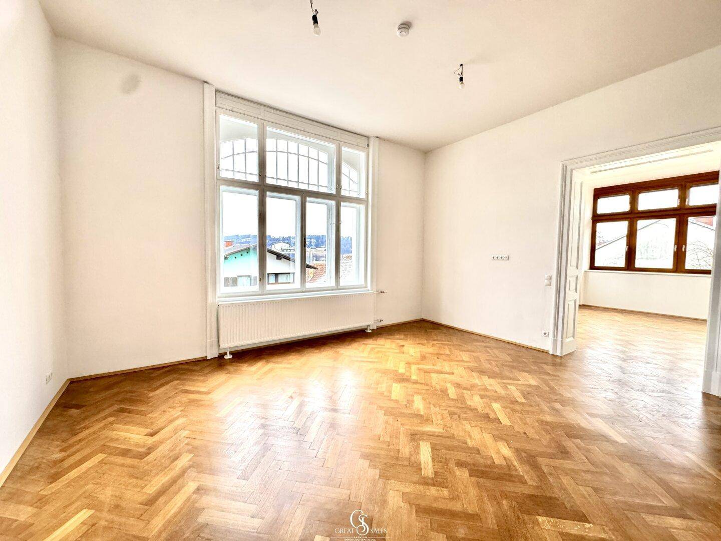 Geräumiger Raum mit Fischgrätparkett und großen Fenstern, die einen weiten Blick bieten.