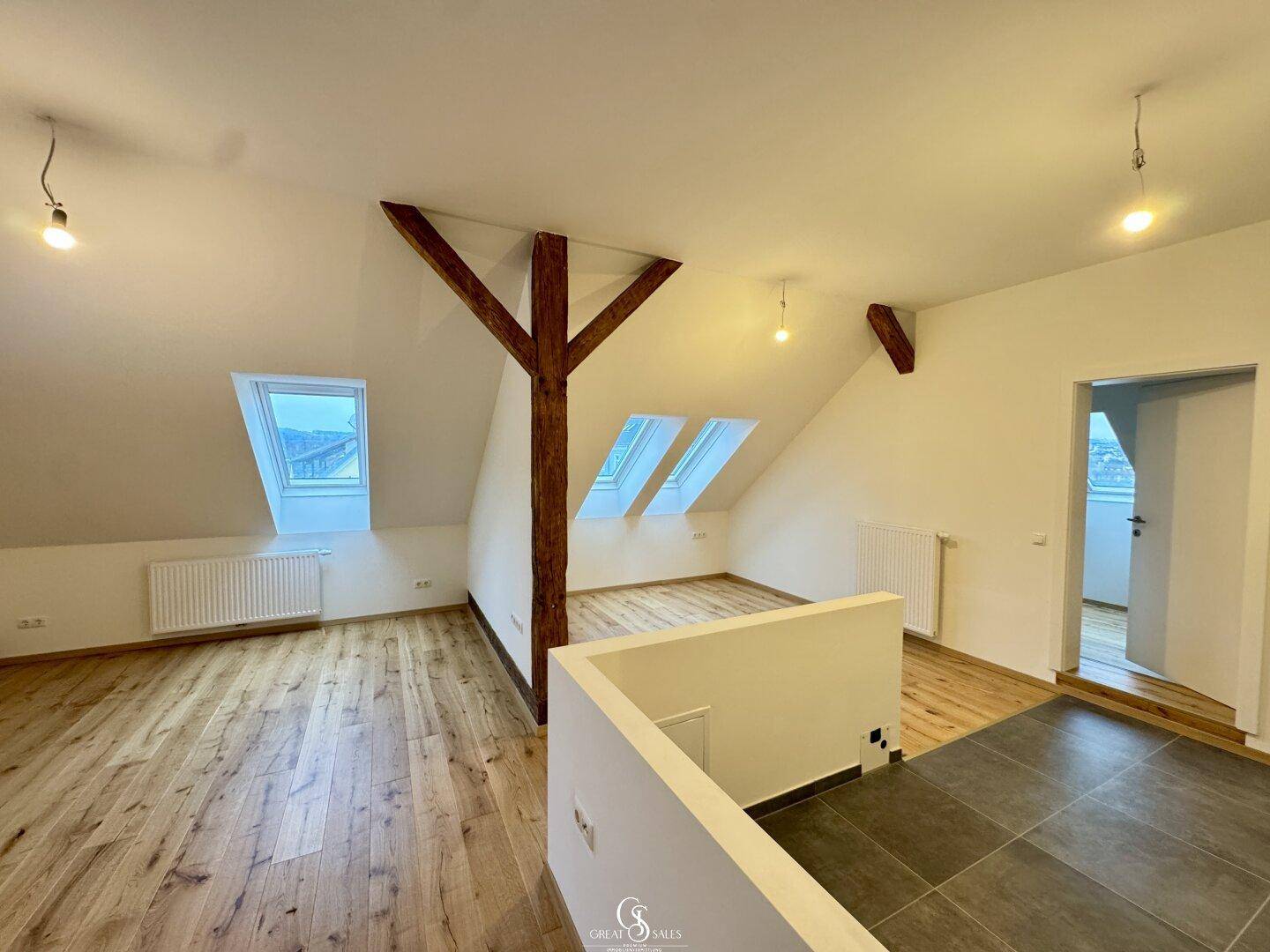 Dachgeschossraum mit sichtbaren Holzbalken, Dachschrägen und mehreren Dachfenstern für viel Licht.