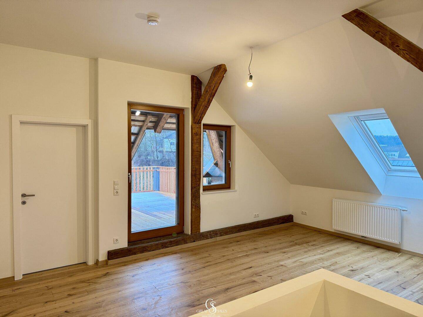 Heller Dachgeschossraum mit Holzbalken und Zugang zu einem Balkon, bietet einen schönen Ausblick.