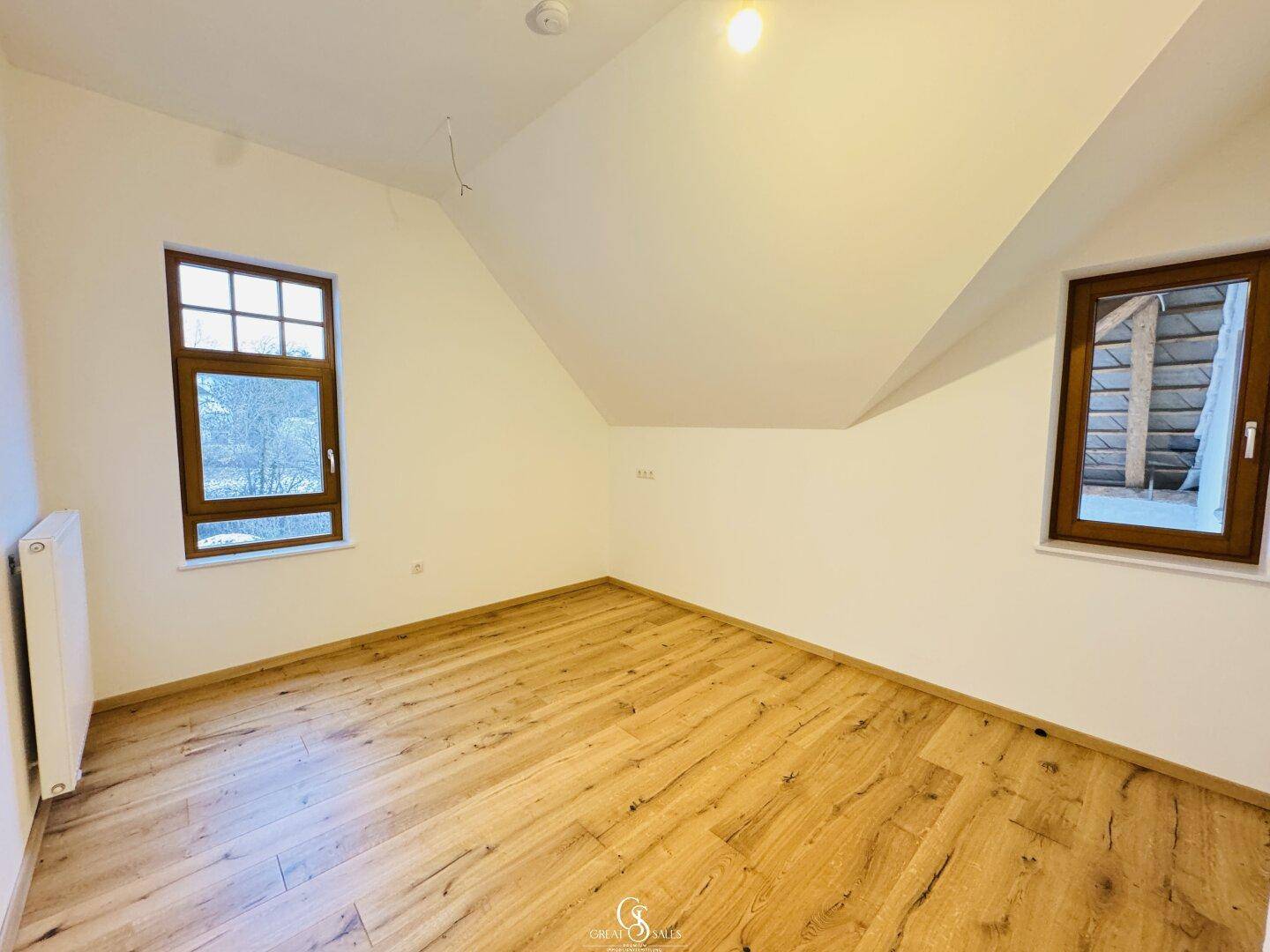 Dachgeschosszimmer mit Holzboden und zwei Fenstern, bietet eine helle und ruhige Atmosphäre.