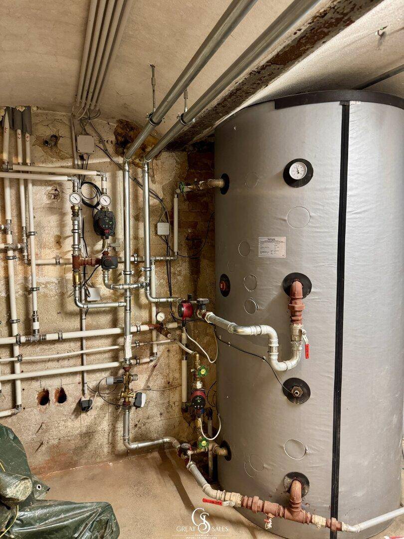 Heizungsraum mit großem Warmwasserspeicher und komplexer Rohrinstallation.