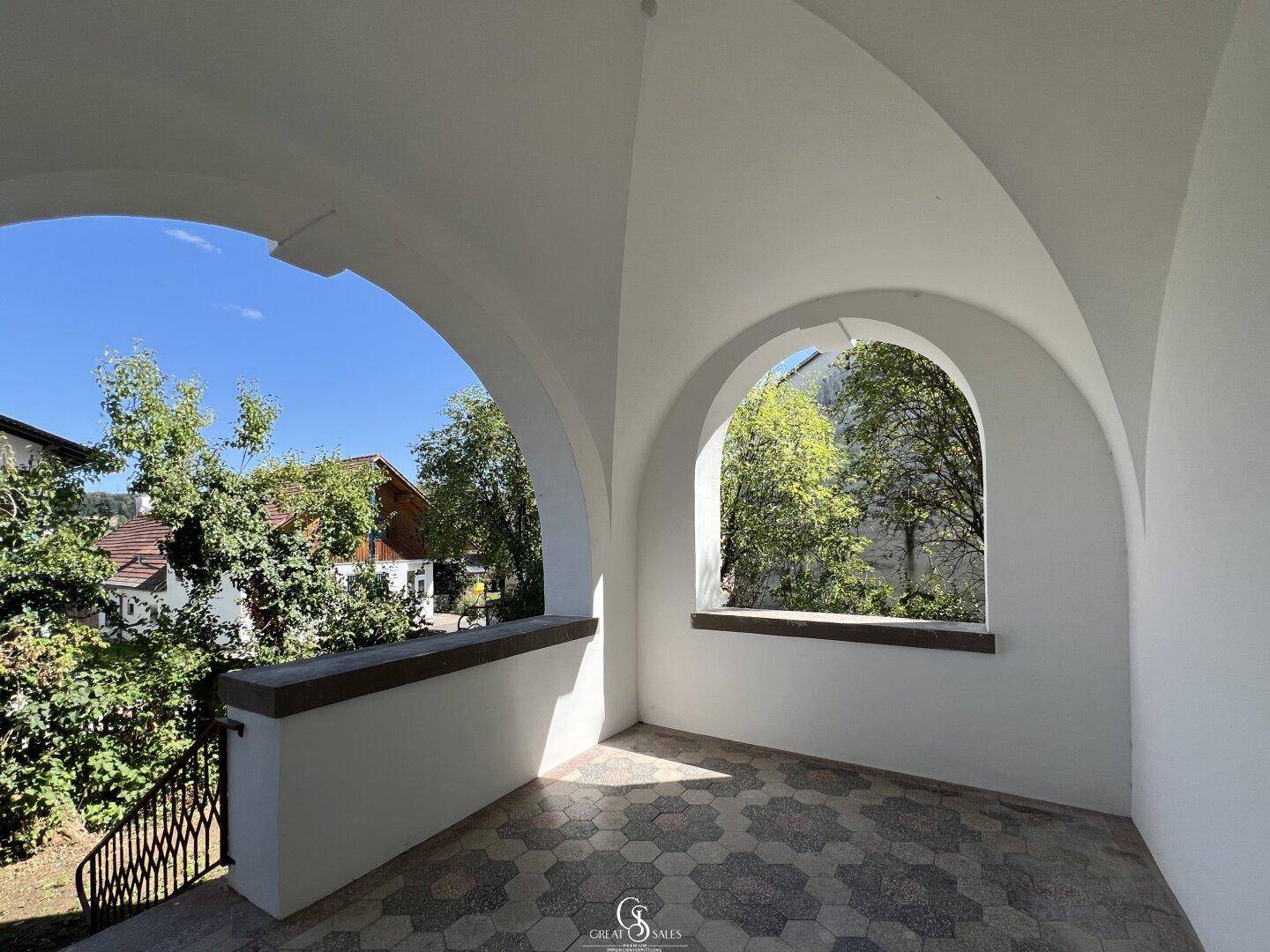 Überdachte Loggia mit gewölbten Bögen und gemusterten Fliesen, bietet einen Blick ins Grüne.