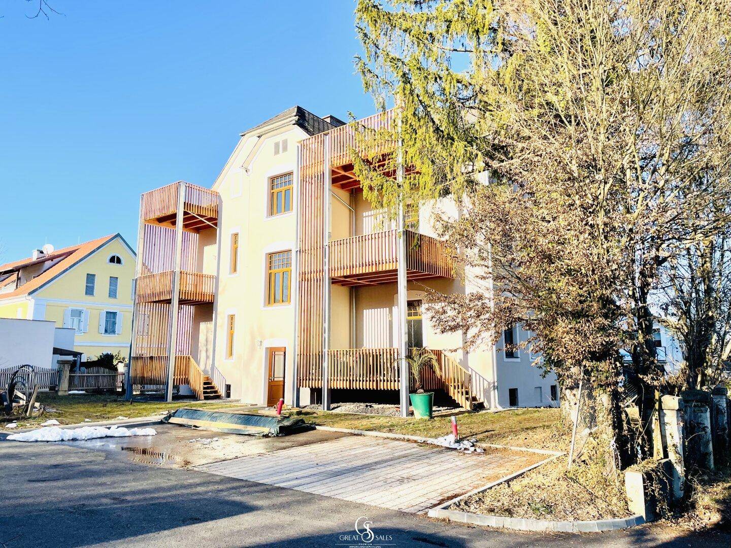 Seitenansicht des Gebäudes mit modernen Holzverkleidungen und mehreren Balkonen, umgeben von Natur.