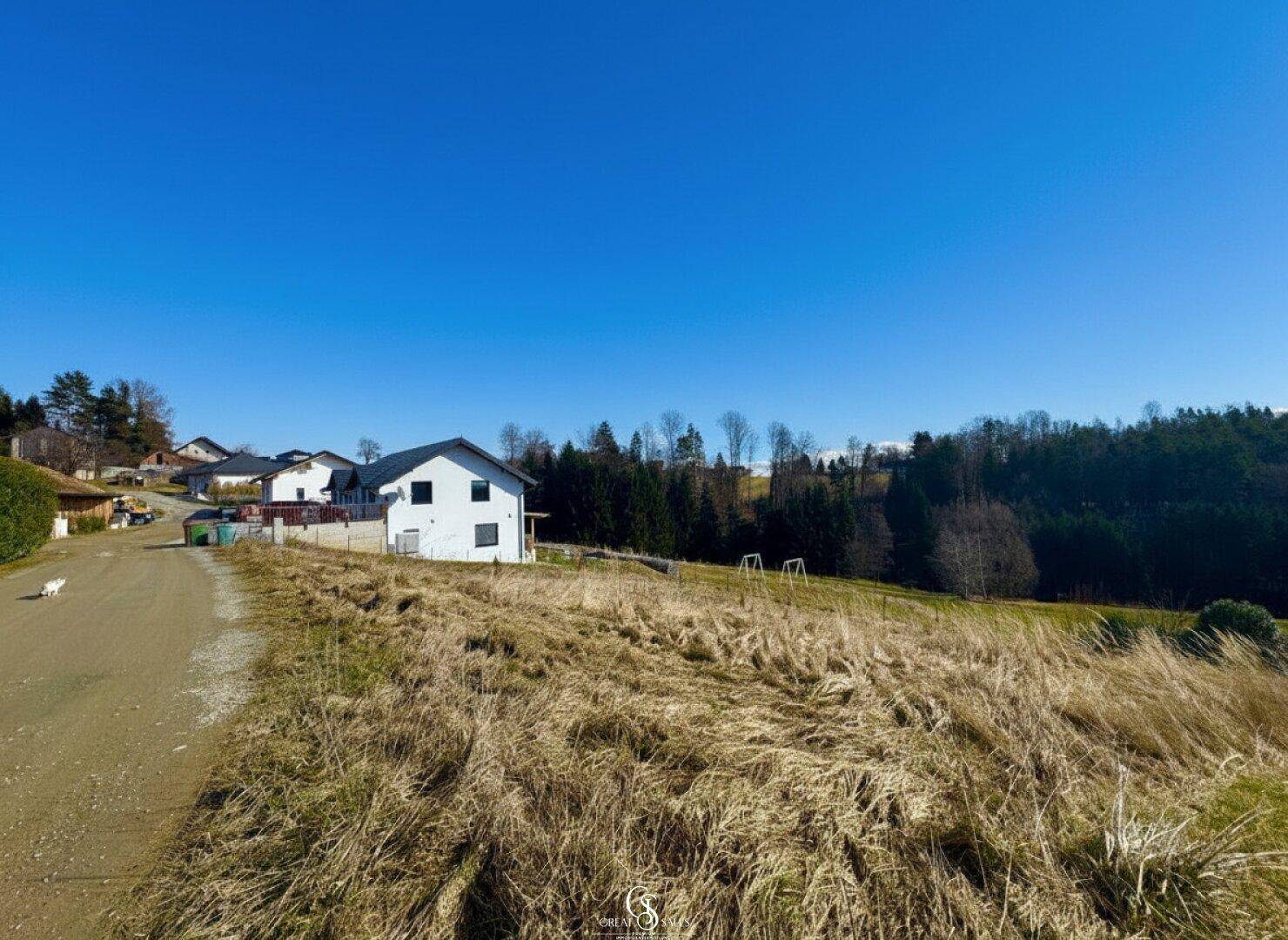Blick auf Wohnhäuser in ländlicher Umgebung mit weiten Feldern und blauem Himmel.