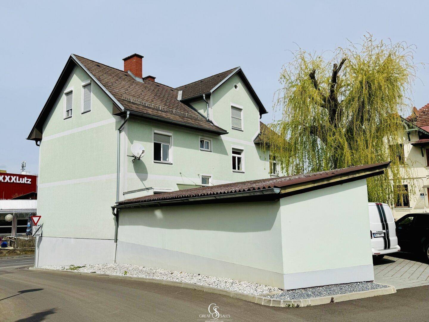 Seitenansicht des Gebäudes mit hellgrüner Fassade, Satteldach und angrenzender Straße.
