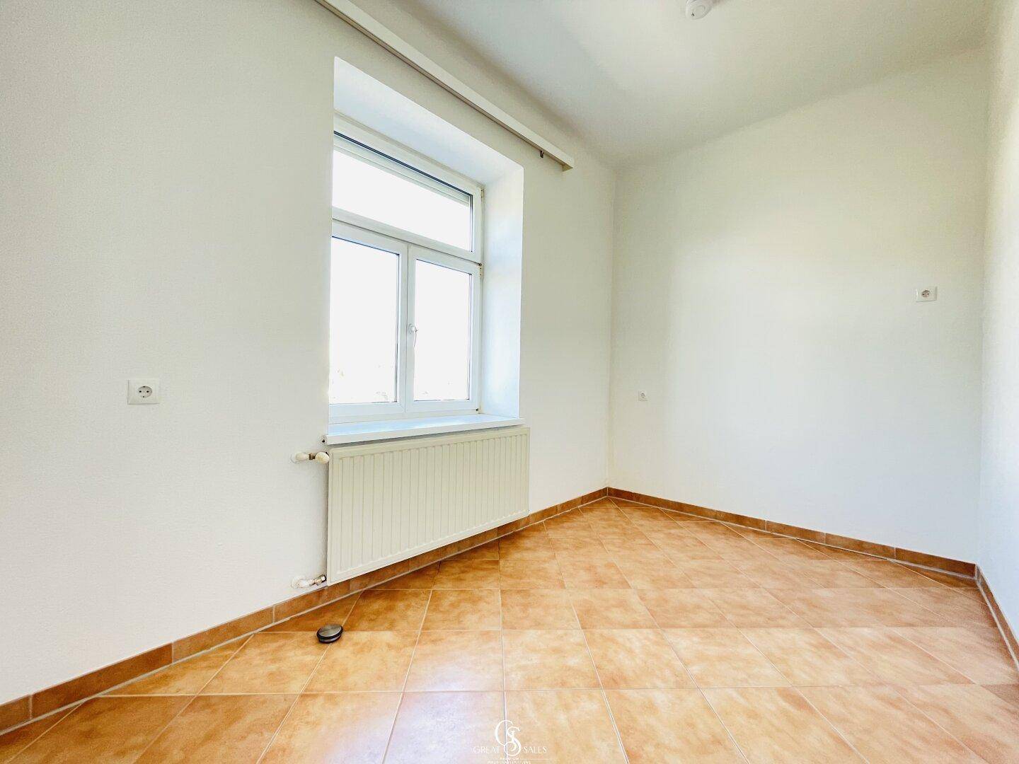 Helles Zimmer mit Terrakotta-Fliesenboden, weiß gestrichenen Wänden und einem Fenster.