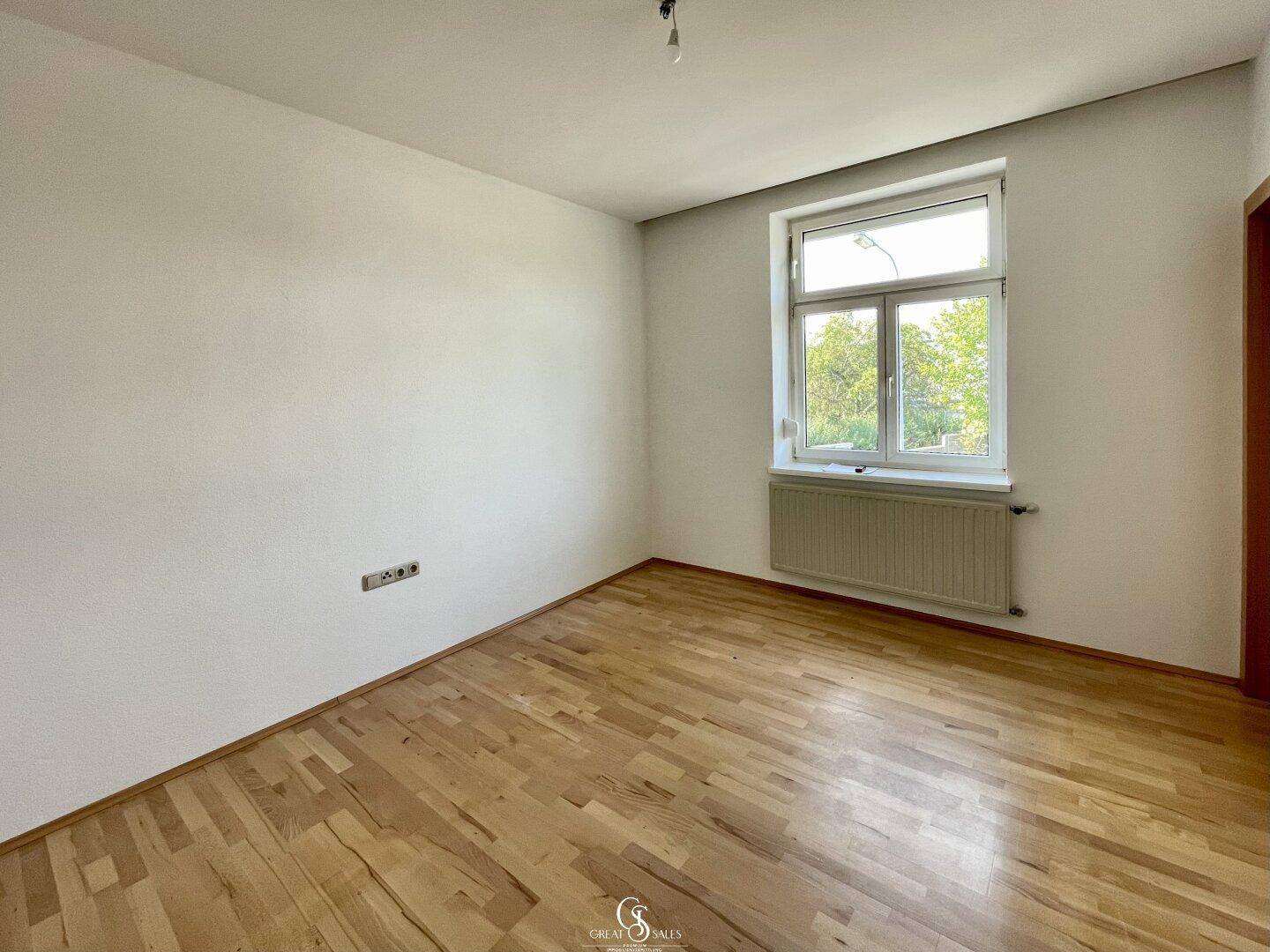 Helles Schlafzimmer mit Holzparkettboden, weiß gestrichenen Wänden und einem großen Fenster.