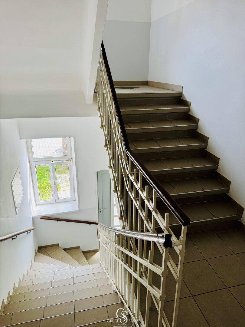 Geräumiges Treppenhaus mit gefliesten Stufen, Fenster und klassischem Geländer.