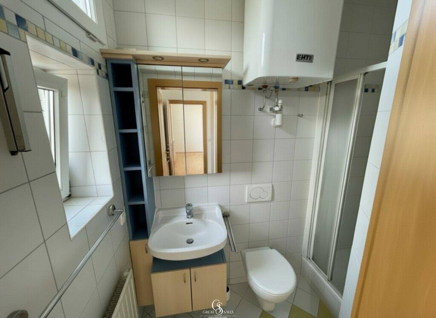 Gefliestes Badezimmer mit Dusche, Waschbecken, Toilette und Fenster für natürliche Belüftung.