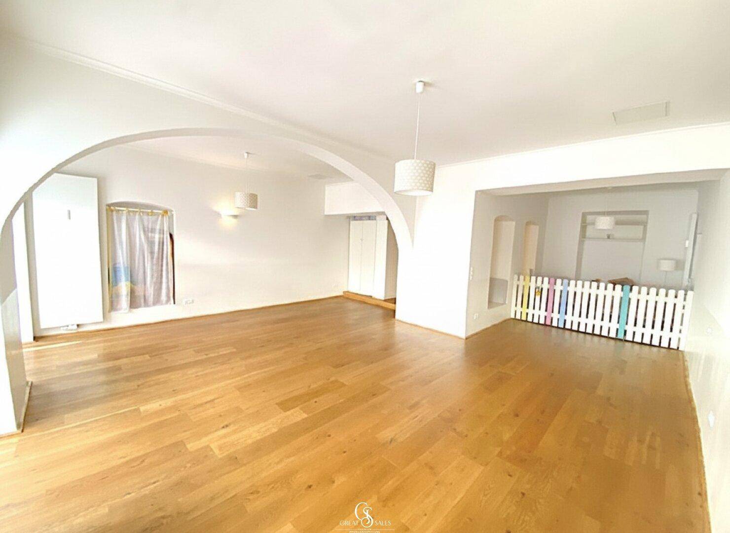 Geräumiger, heller Innenraum mit Holzboden, weißen Wänden und einem dekorativen Zaun im Hintergrund.