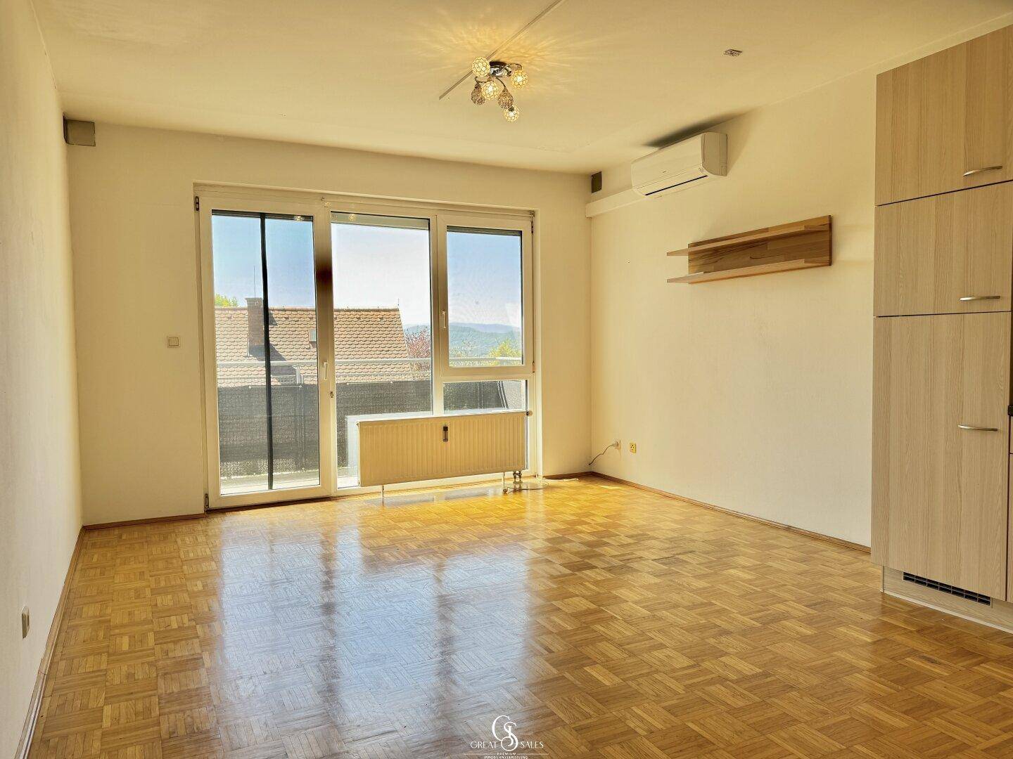 Lichtdurchfluteter Wohnbereich mit Parkettboden und großem Fenster, das viel Tageslicht hereinlässt.
