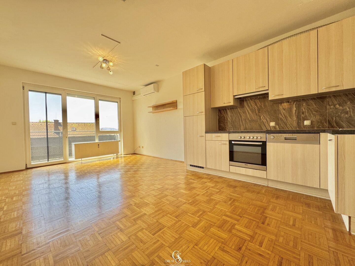 Heller Wohnbereich mit integrierter Küchenzeile, Parkettboden und Zugang zum Balkon.