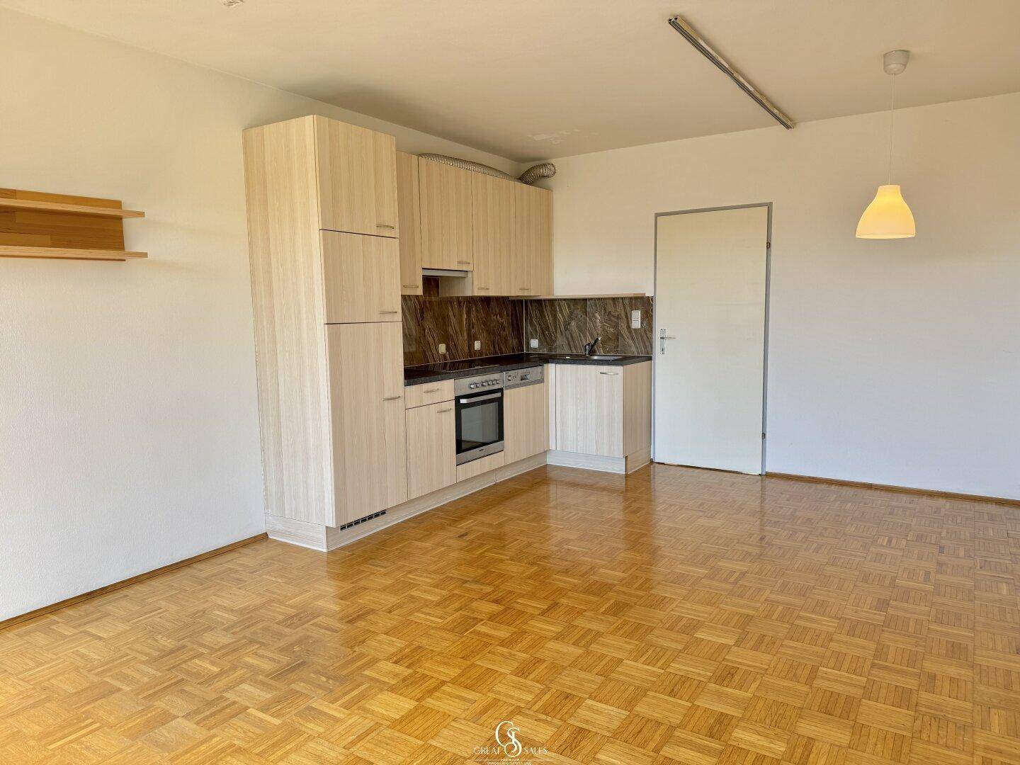 Kompakte Küchenzeile mit hellen Holzfronten und modernen Geräten, integriert in den Wohnbereich.