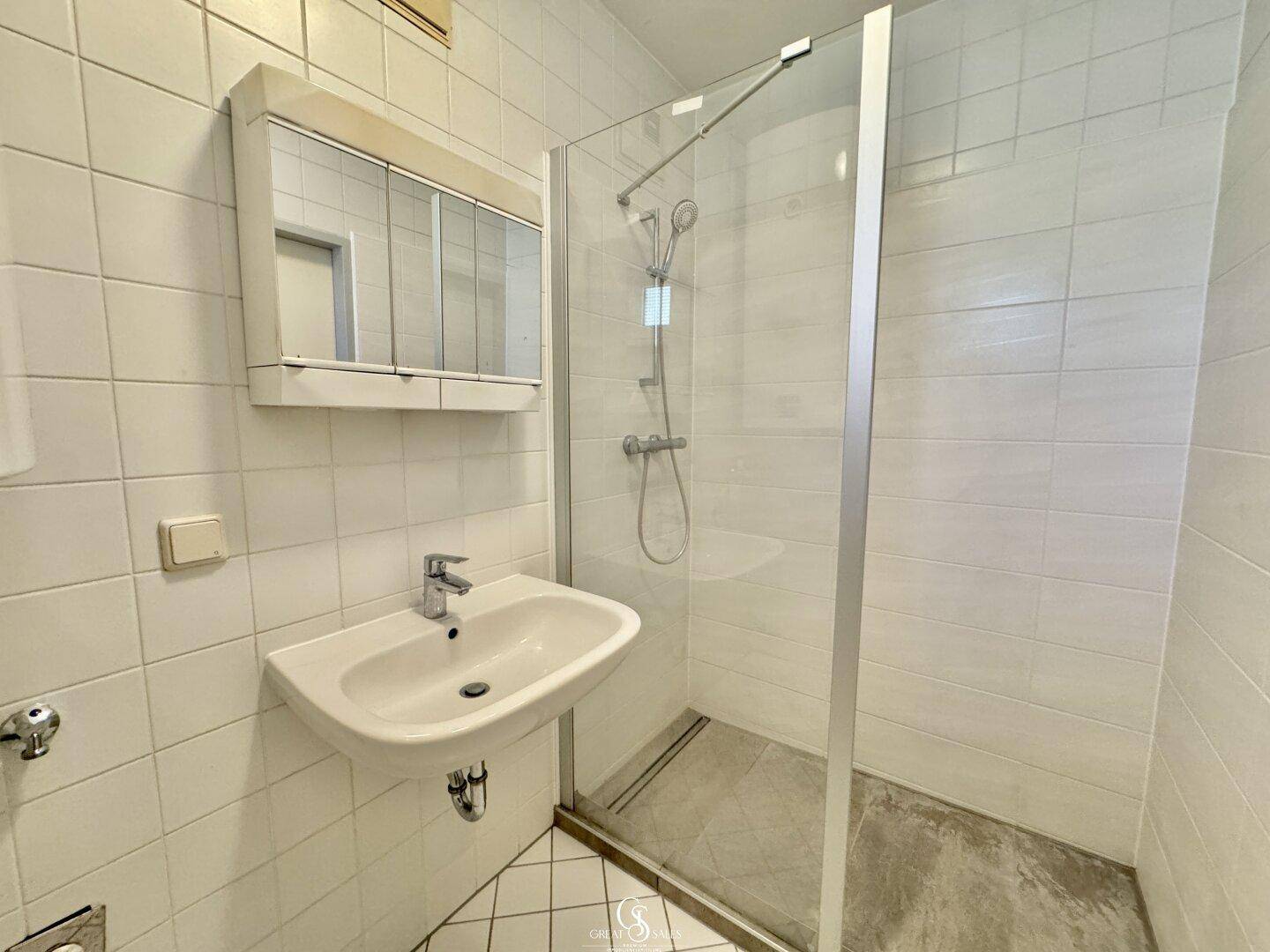 Helles Badezimmer mit Dusche, Waschbecken und weißen Fliesen, funktional und sauber.