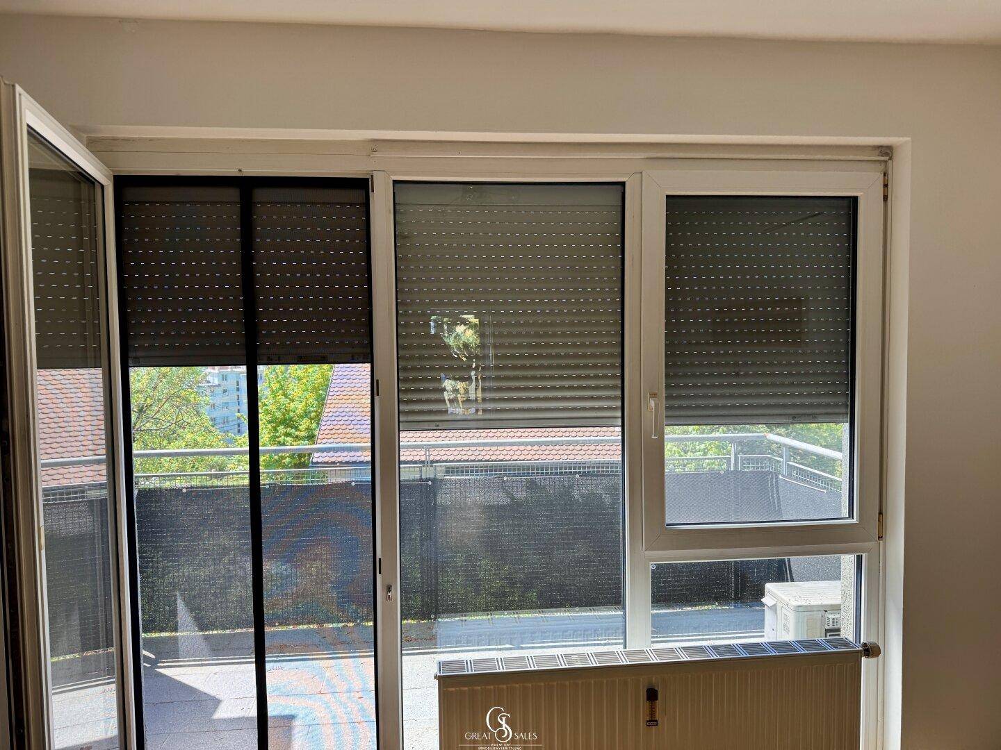 Großes Fenster mit Rollläden und Blick ins Grüne, sorgt für Privatsphäre und Sonnenschutz.