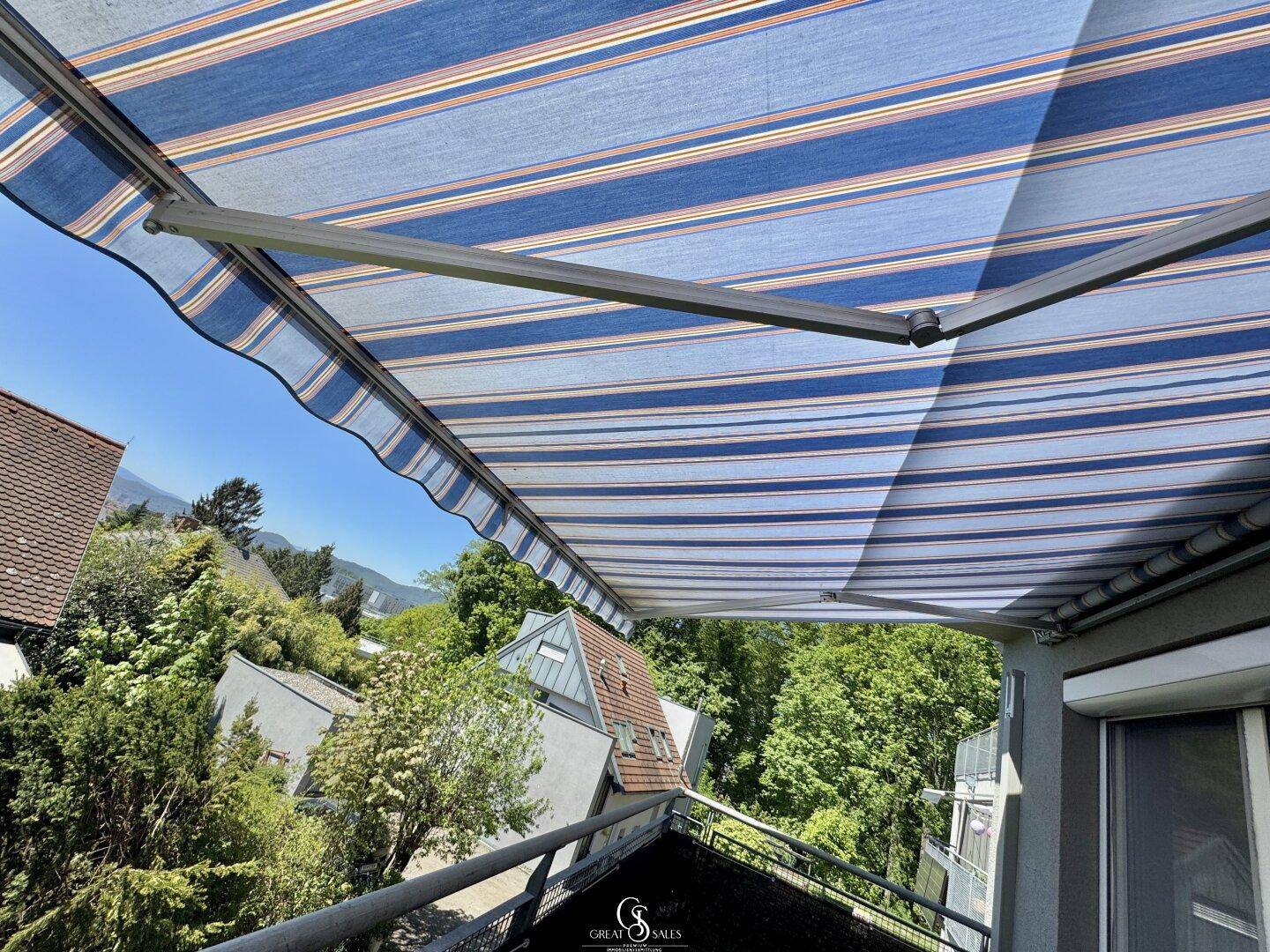 Geräumiger Balkon mit gestreifter Markise und weitem Blick ins Grüne an einem sonnigen Tag.