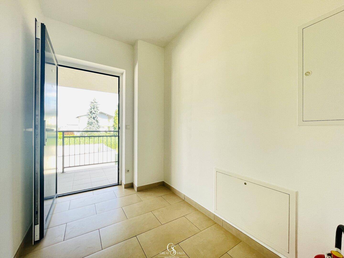 Heller Eingangsbereich mit Fliesenboden und Zugang zu einem sonnigen Balkon.