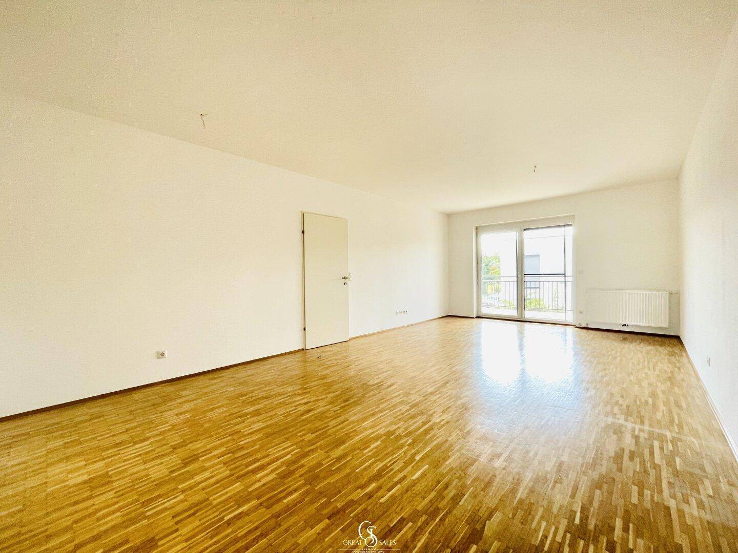 Helles Wohnzimmer mit Parkettboden und großem Fenster, das viel Tageslicht hereinlässt.