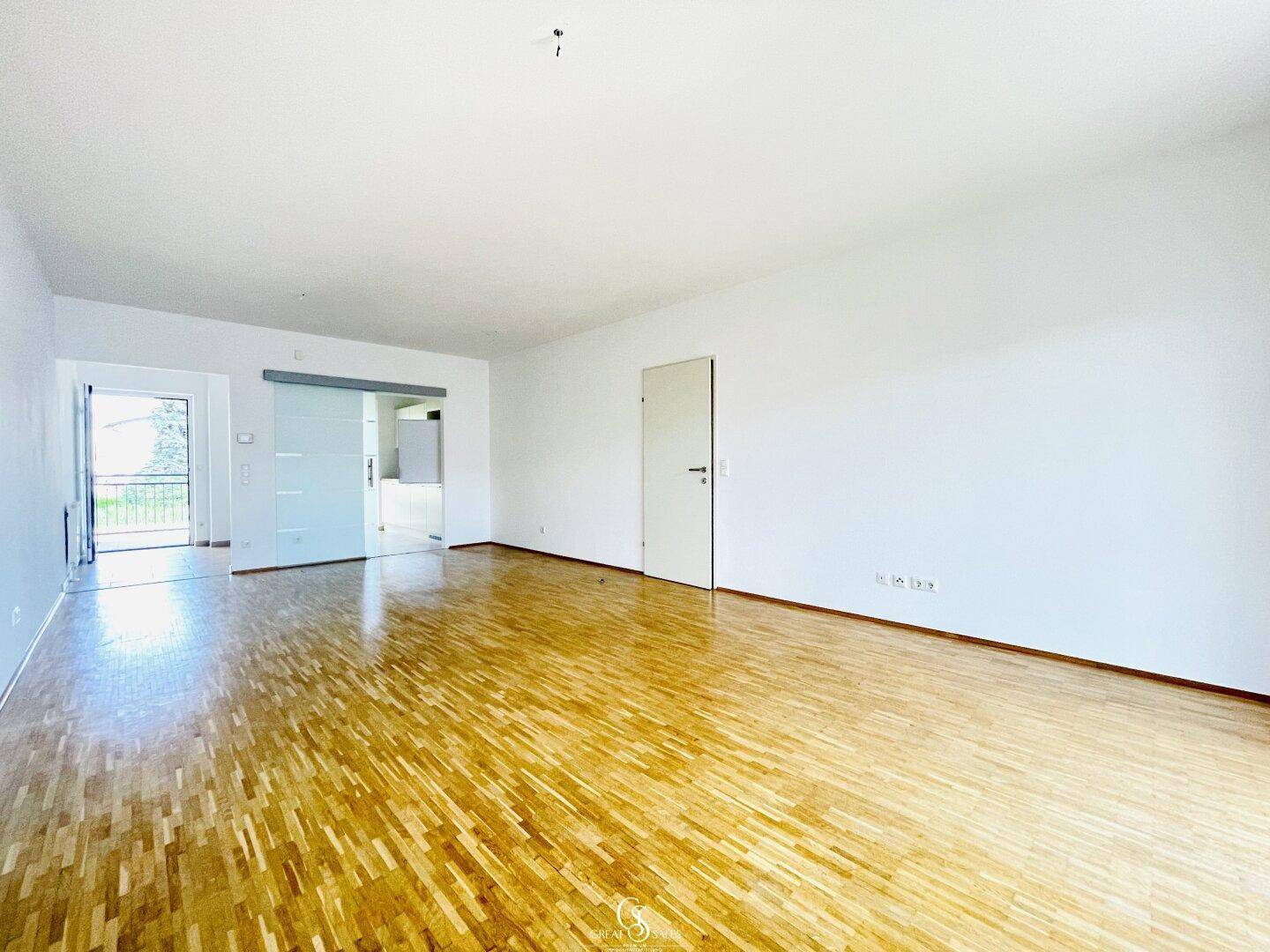 Geräumiges Wohnzimmer mit hellem Parkettboden und einer modernen Glasschiebetür.