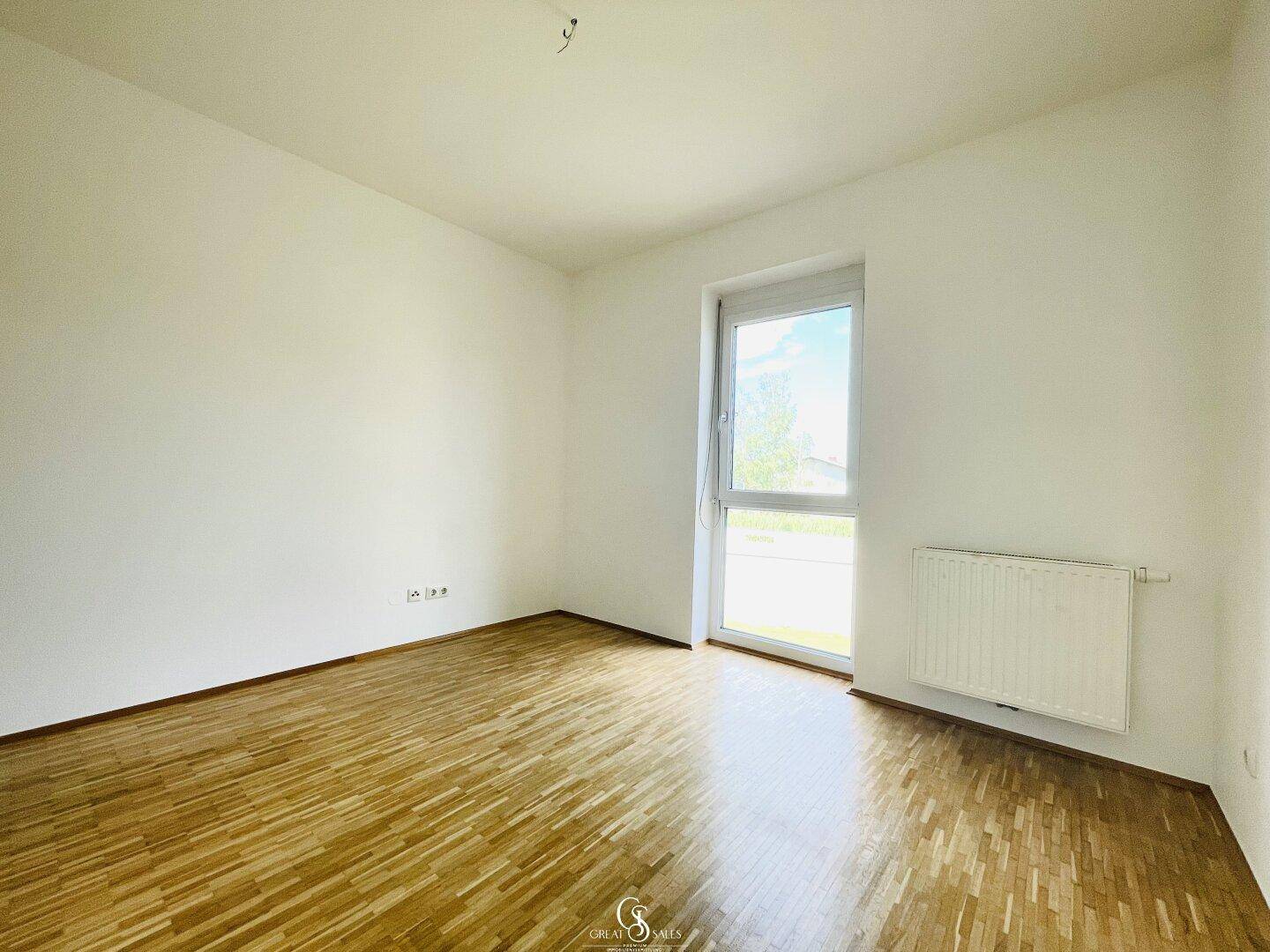 Helles Schlafzimmer mit Parkettboden und großem Fenster, das viel Licht spendet.